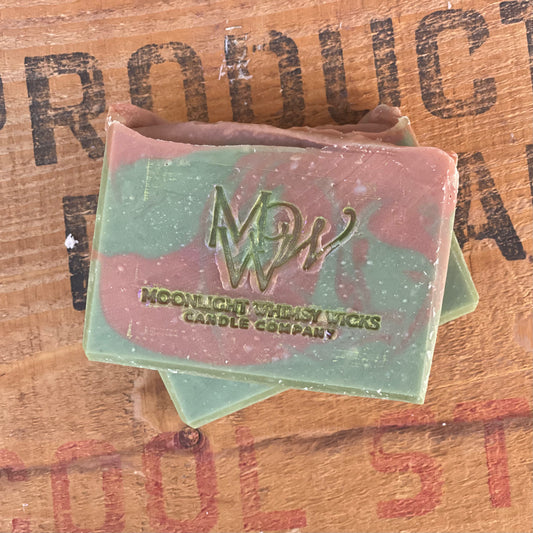 Two soap bars with a green and brown swirl with a visible brand logo on a wooden background