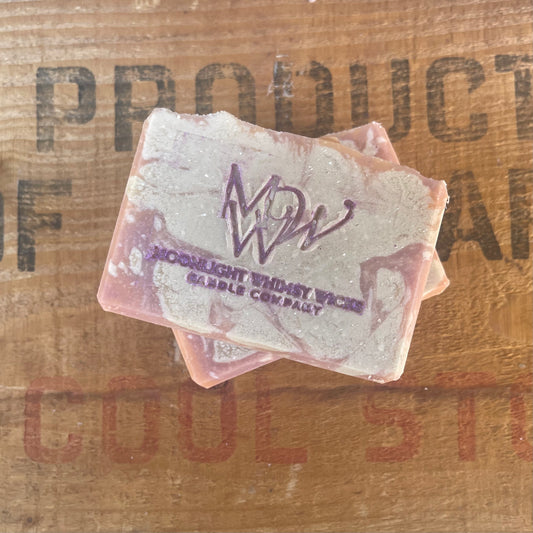 Bar of handmade, artisan soap in cream and orange with a purple 'MW' branding on a wooden crate background