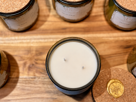 Moonlight Whimsy Wicks double wick Olive Oil wax candle in a recycled green glass jar with cork lids on a rustic wooden tabletop.
