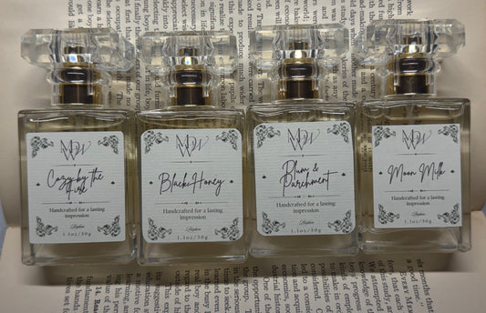 Moonlight Whimsy Wicks Cozy by the Fire, Black Honey, Plum & Parchment, and Moon Milk fall perfumes displayed on open book pages.