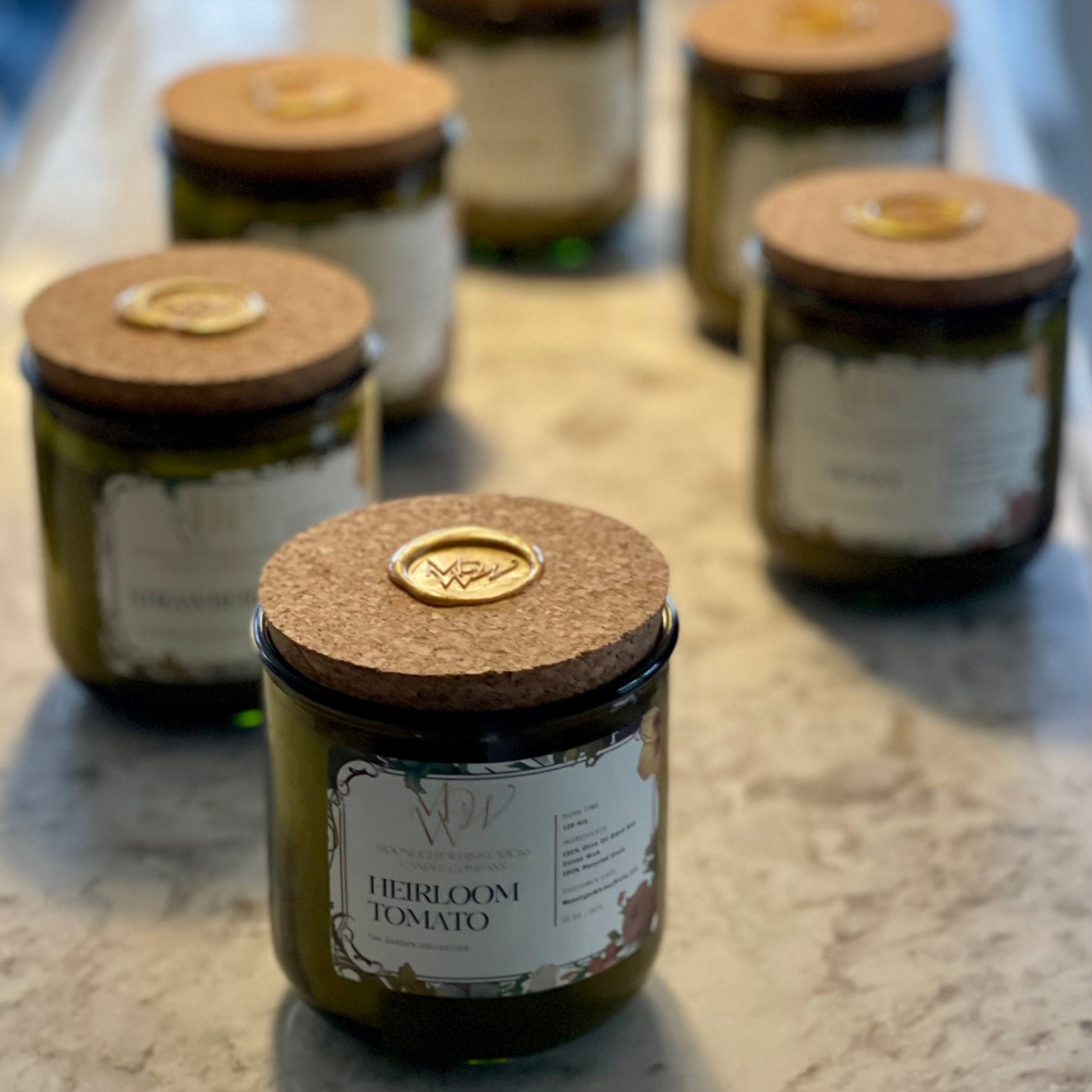 Group of eco-luxe candles from Moonlight Whimsy Wicks’ Garden Collection, displayed on a stone countertop. Each candle is hand-poured in a green recycled glass vessel with a cork lid sealed in gold wax. Ideal for showcasing artisanal, sustainable garden-inspired home fragrances.