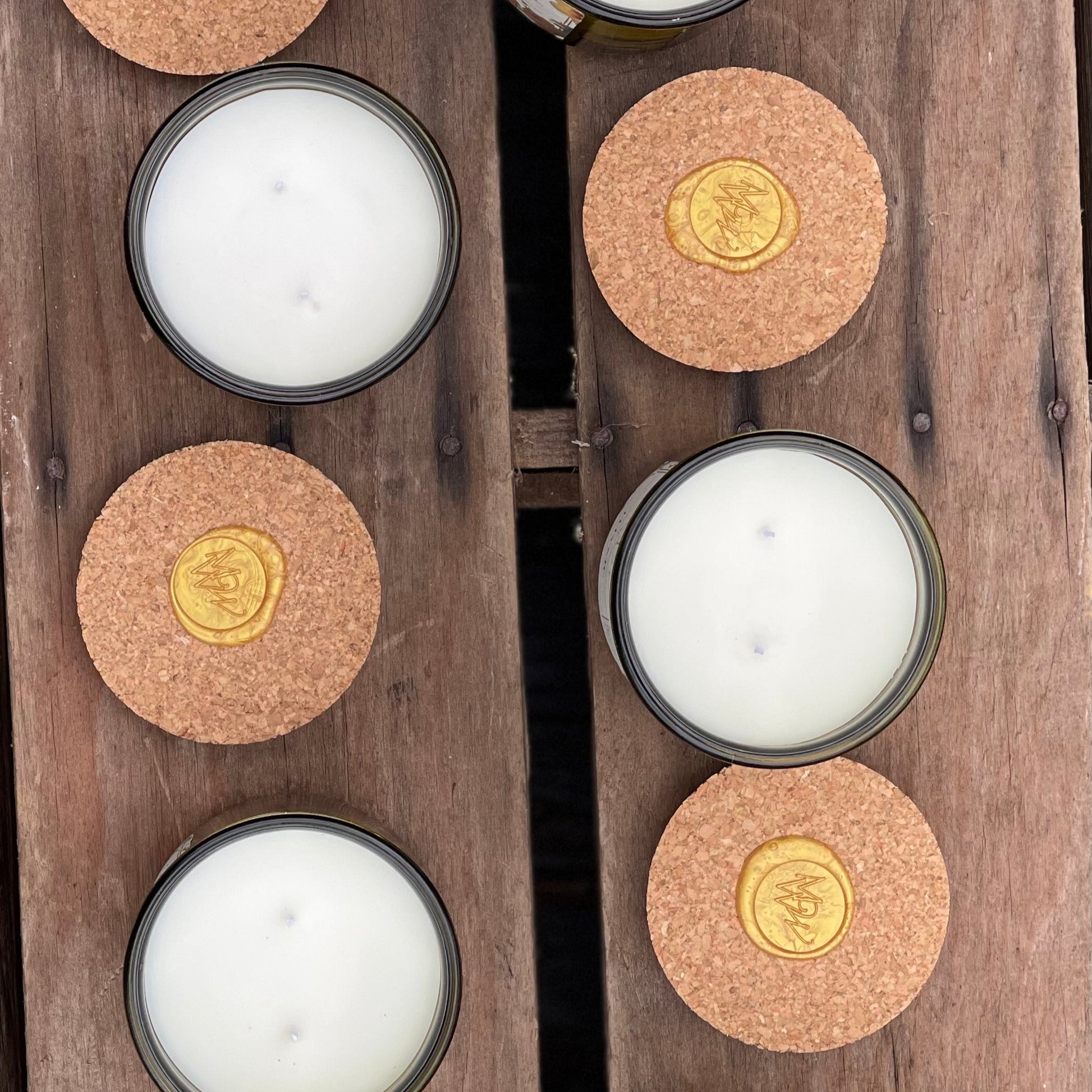 Top-down view of Moonlight Whimsy Wicks' Garden Collection candles featuring creamy white olive oil wax, double wicks, and cork lids with gold wax seals. Set on a rustic wooden surface, these eco-conscious candles in green glass vessels highlight artisanal craftsmanship and sustainable luxury.