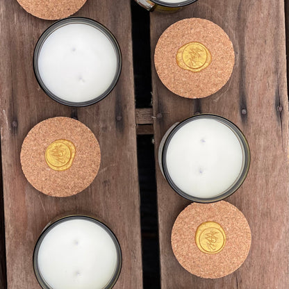 Top-down view of Moonlight Whimsy Wicks' Garden Collection candles featuring creamy white olive oil wax, double wicks, and cork lids with gold wax seals. Set on a rustic wooden surface, these eco-conscious candles in green glass vessels highlight artisanal craftsmanship and sustainable luxury.