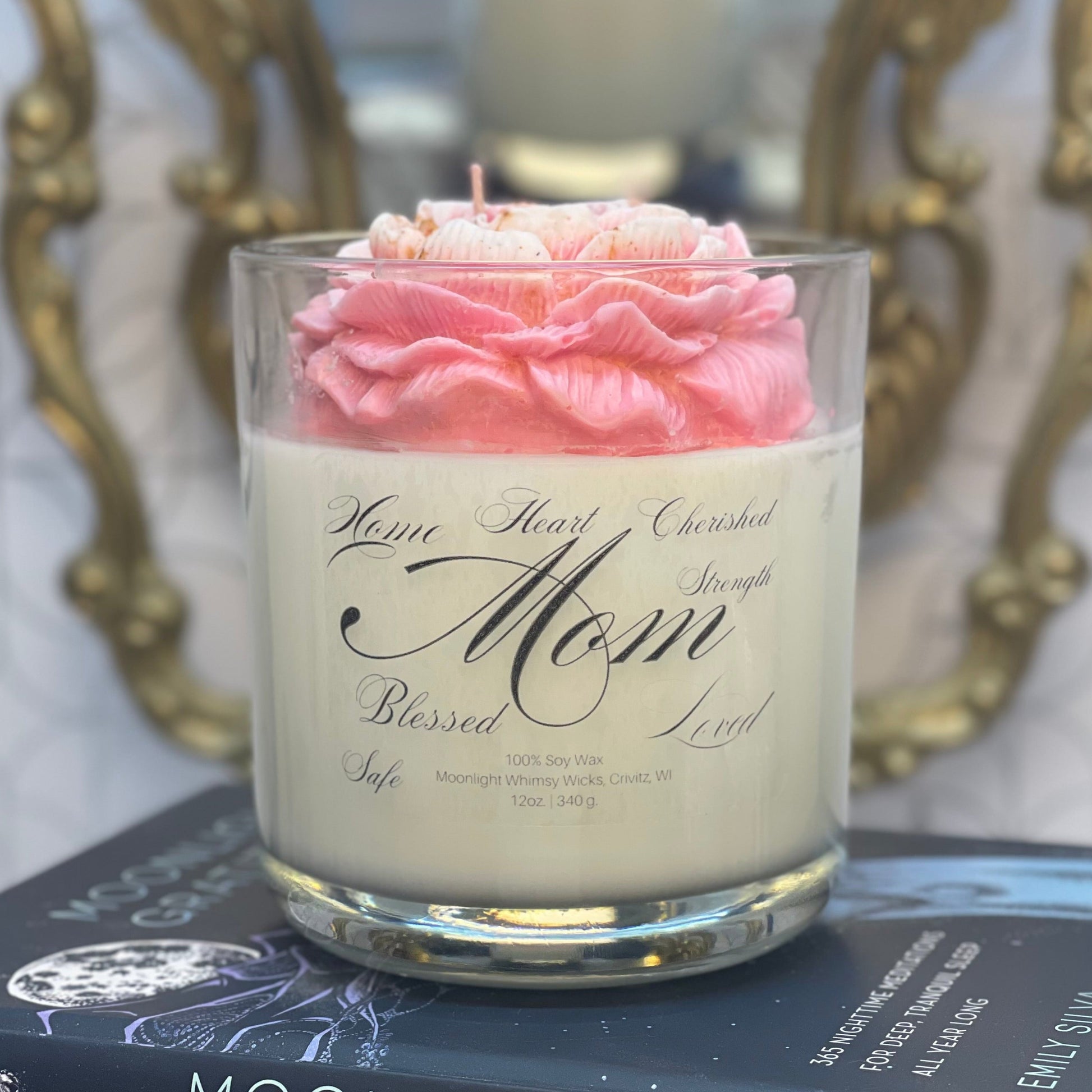Candle in a glass jar with pink rose on top, placed on books with decorative background