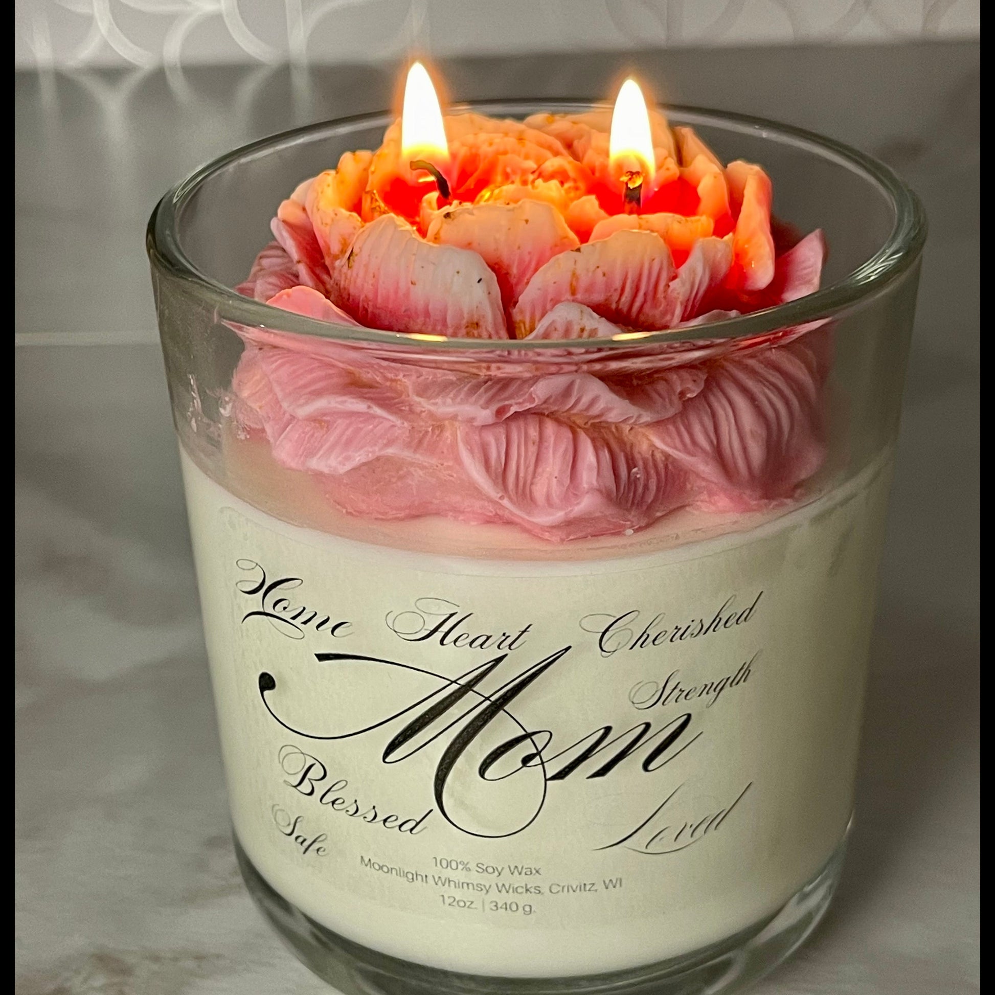 Candle in a glass jar with pink flowers and a sentimental message on a marble surface.