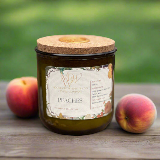 Peaches Candle from Moonlight Whimsy Wicks’ Garden Collection, styled in a green recycled glass jar with a cork lid and floral label, surrounded by fresh peaches on a rustic wooden surface with a blurred green garden background. Hand-poured with olive oil wax for a fruity, summer-inspired scent.
