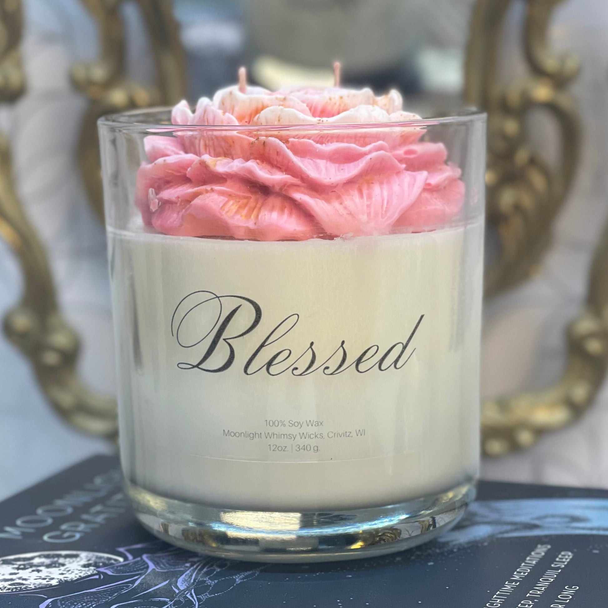 Candle in a glass jar with pink flowers labeled 'Blessed' on top of books.