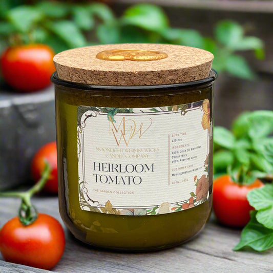 Heirloom Tomato Candle from The Garden Collection by Moonlight Whimsy Wicks. Hand-poured in a recycled green glass jar with a cork lid, this olive oil wax candle features a botanical label and sits among fresh vine-ripened tomatoes and lush green leaves. Perfect for garden lovers and eco-friendly candle enthusiasts seeking a fresh, earthy scent.