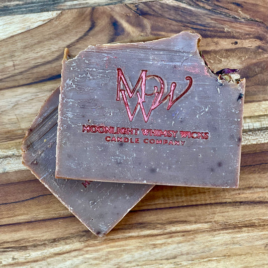 Handcrafted rose clay artisan soap bar from Moonlight Whimsy Wicks, stamped with a red foil logo and topped with dried botanicals. Cold processed, natural soap made in small batches with moisturizing oils and gentle clays for radiant, sensitive skin.  Fragrance is inspired by BBW Dark Kiss
