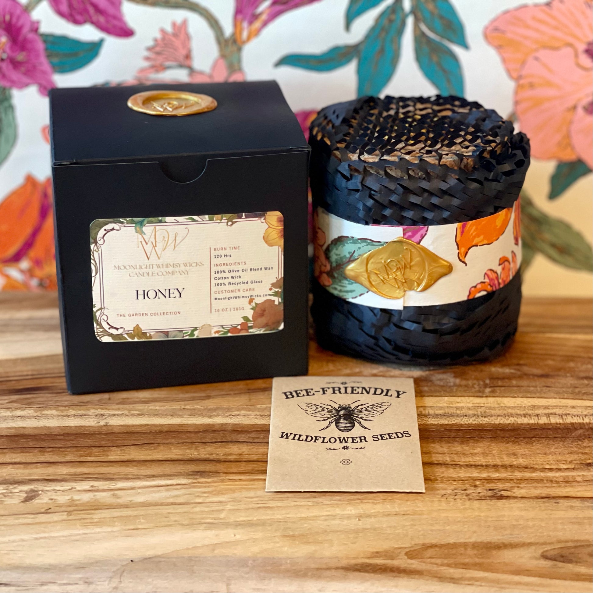 Moonlight Whimsy Wicks Honey Candle gift set featuring a black eco-luxe box with floral label and wax seal, a hand-wrapped candle in dark braided fiber with gold wax stamp, and a packet of bee-friendly wildflower seeds. Perfect for sustainable gifting, garden lovers, and artisanal candle collectors.