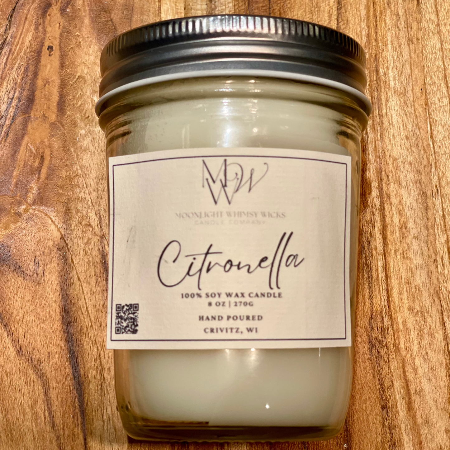 Close up of a canning jar soy wax candle with silver lid labeled Citronella on a rustic wood background