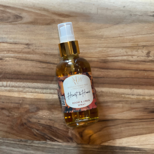 Bottle of 'Heart & Home' room and linen spray by Moonlight Whimsy Wicks on a wooden surface