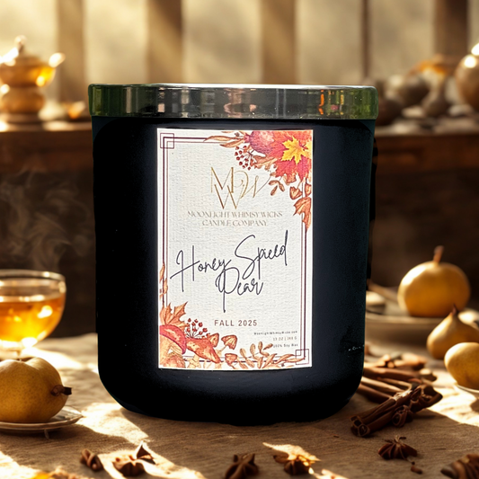 Honey Spiced Pear candle by Moonlight Whimsy Wicks, in a matte black jar with red, orange and yellow leaves on label, surrounded by fresh pears, honey, cinnamon sticks, and autumn light.