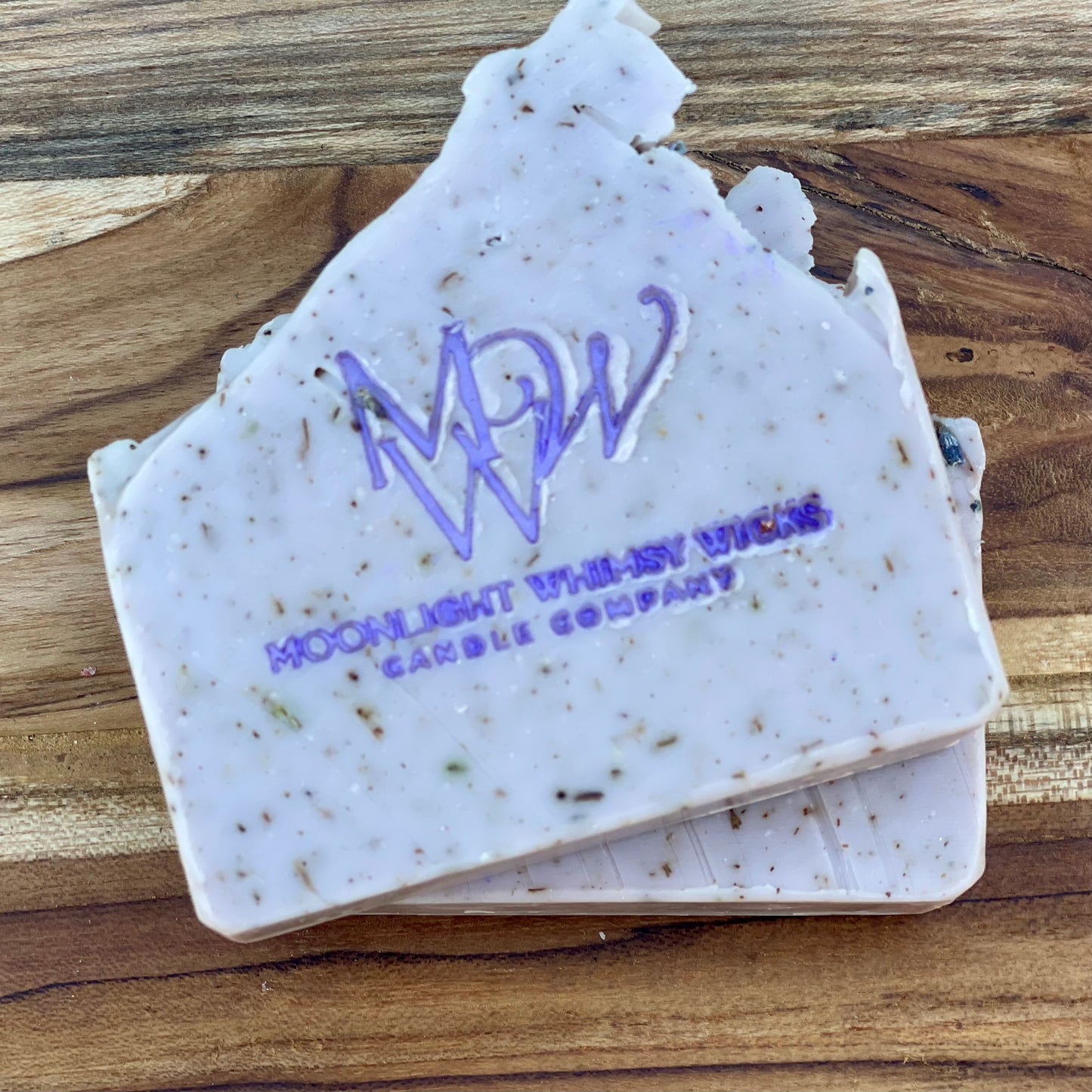 Close-up of Moonlight Whimsy Wicks handmade lavender soap bar with purple logo, cold processed and infused with natural botanicals and exfoliating herbs. Artisan soap for sensitive skin, crafted in small batches for natural skincare routines