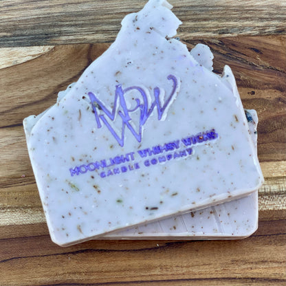 Close-up of Moonlight Whimsy Wicks handmade lavender soap bar with purple logo, cold processed and infused with natural botanicals and exfoliating herbs. Artisan soap for sensitive skin, crafted in small batches for natural skincare routines