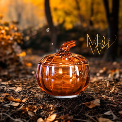Amber glass pumpkin candle on a forest floor with blurred autumn leaves