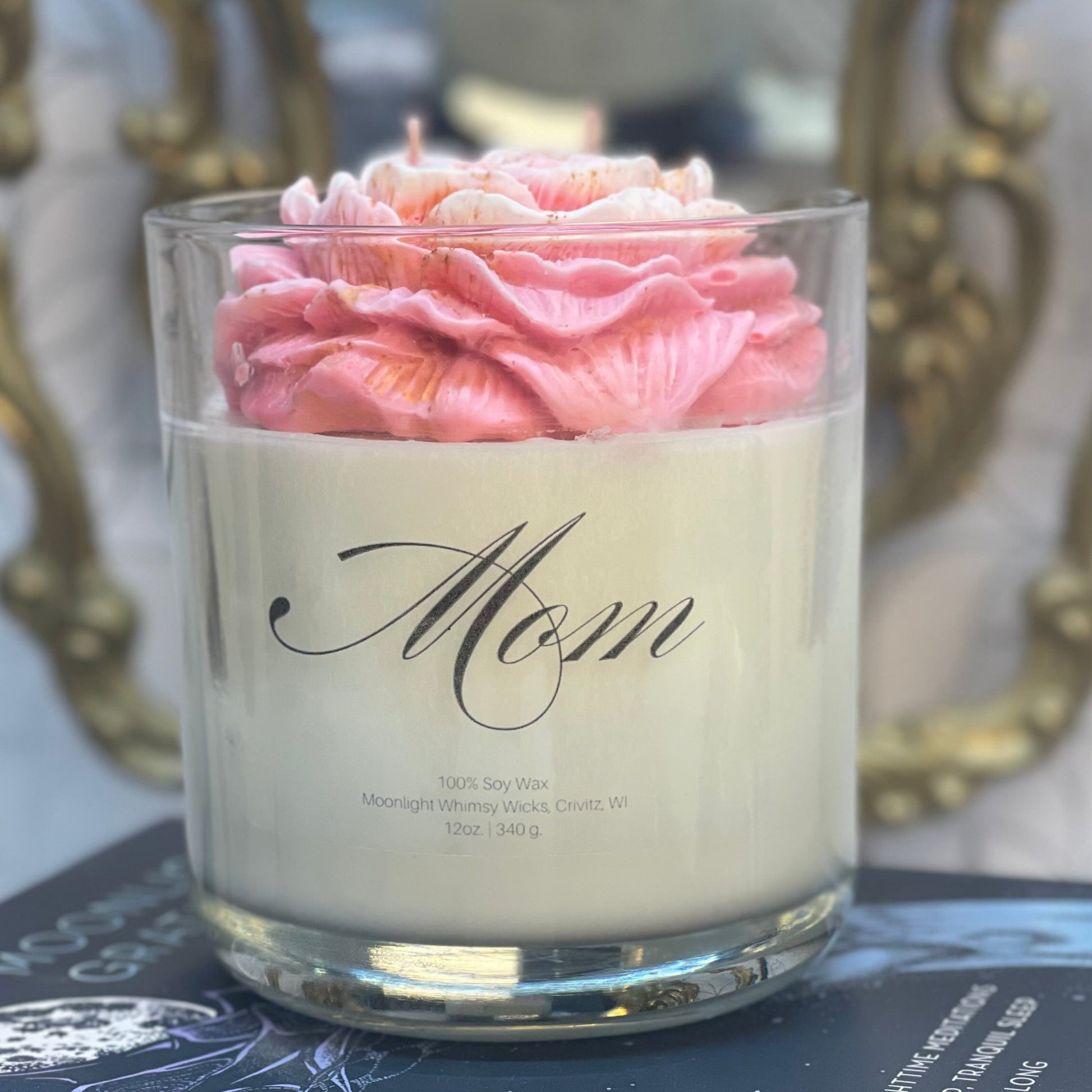 Candle with pink peony in a glass holder on top of books, with decorative background
