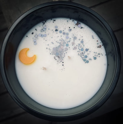 Image of a creamy white soy wax candle with a gold moon embed and black eco glitter in a black matte vessel.  Representative of Moonlight Whimsy Wicks Signature line.