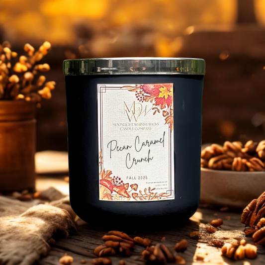 Pecan Caramel Crunch soy candle by Moonlight Whimsy Wicks, in a matte black jar with a fall-themed label, styled on a rustic wood surface surrounded by pecans and golden autumn light.