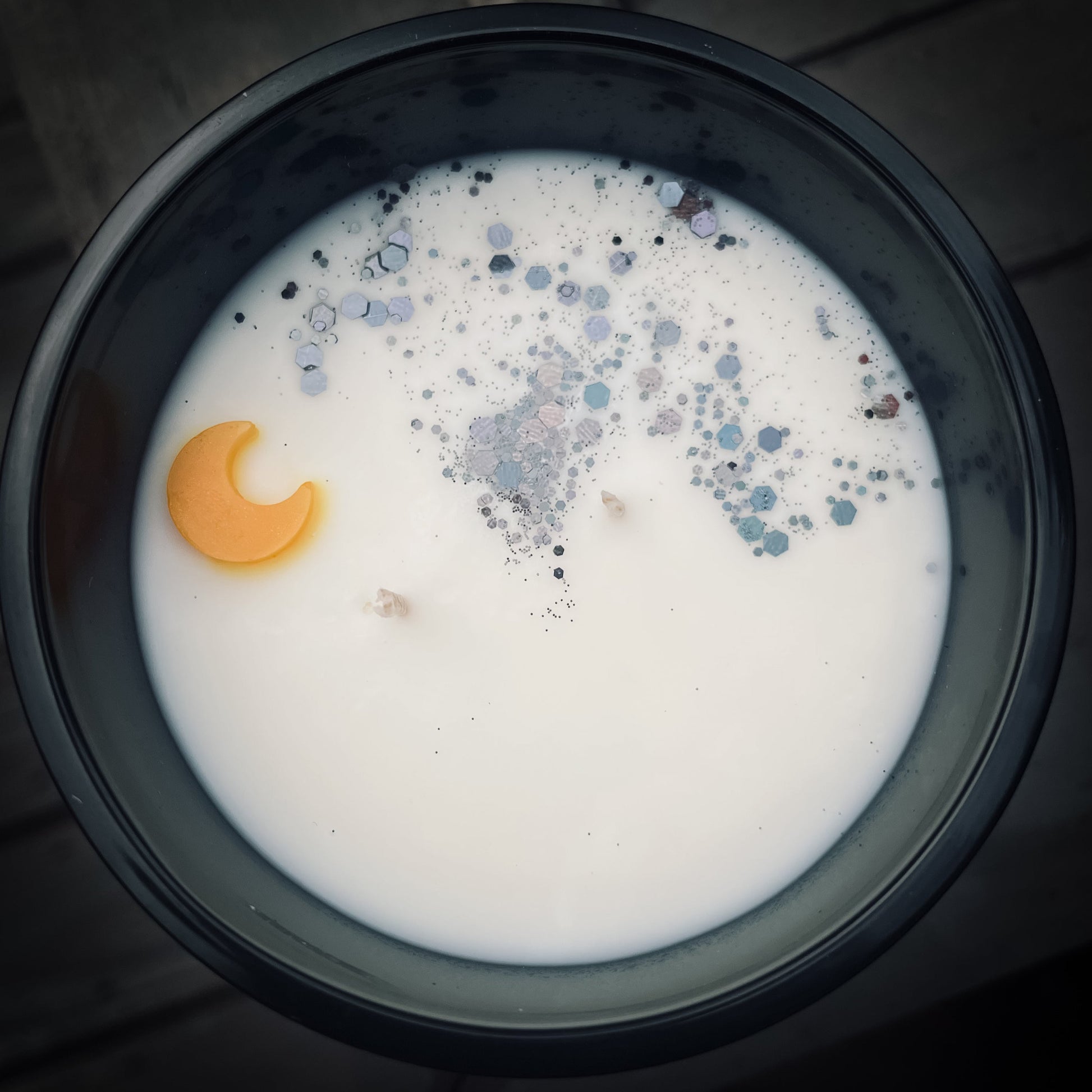 Closeup Image of a soy wax candle with a small yellow moon and black glitter.