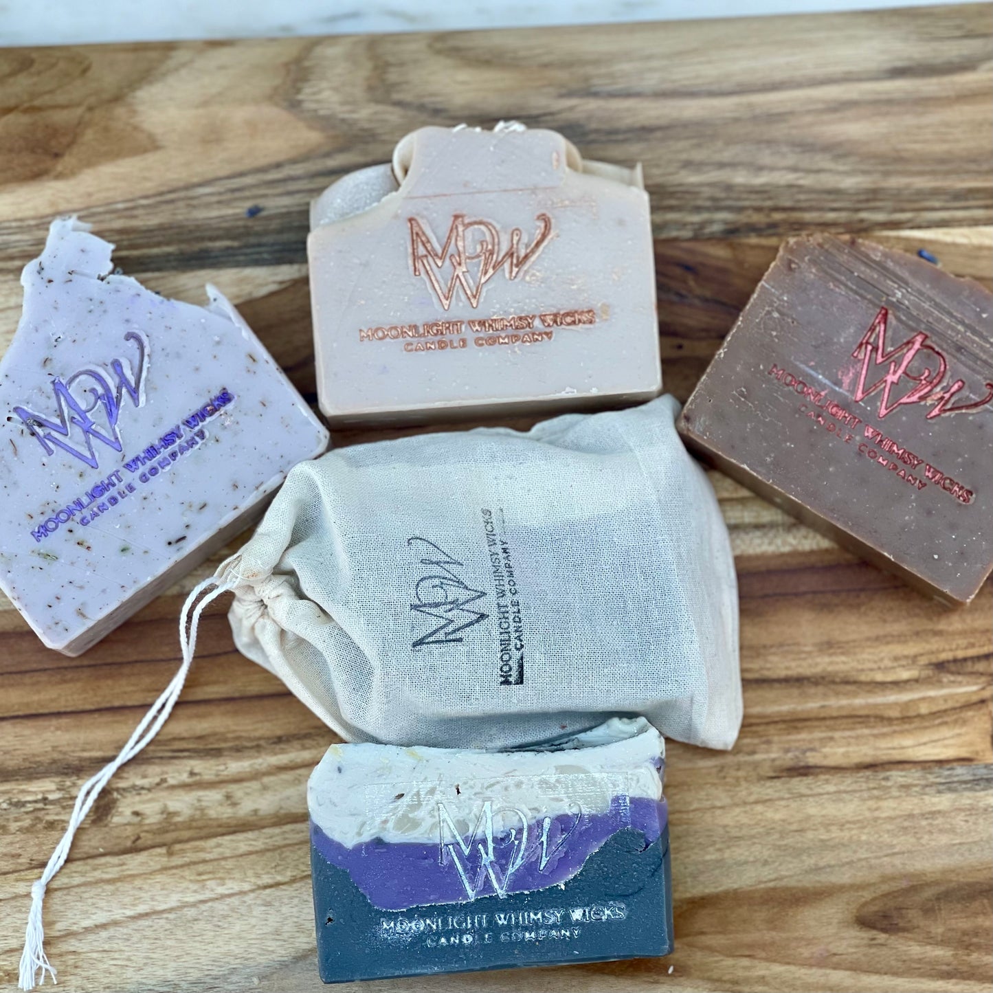 Artisan handmade soap bars from Moonlight Whimsy Wicks displayed on a wooden board, featuring cold processed soap, and a muslin gift bag. Small batch, eco-friendly bar soaps for sensitive skin and luxury skincare routines.