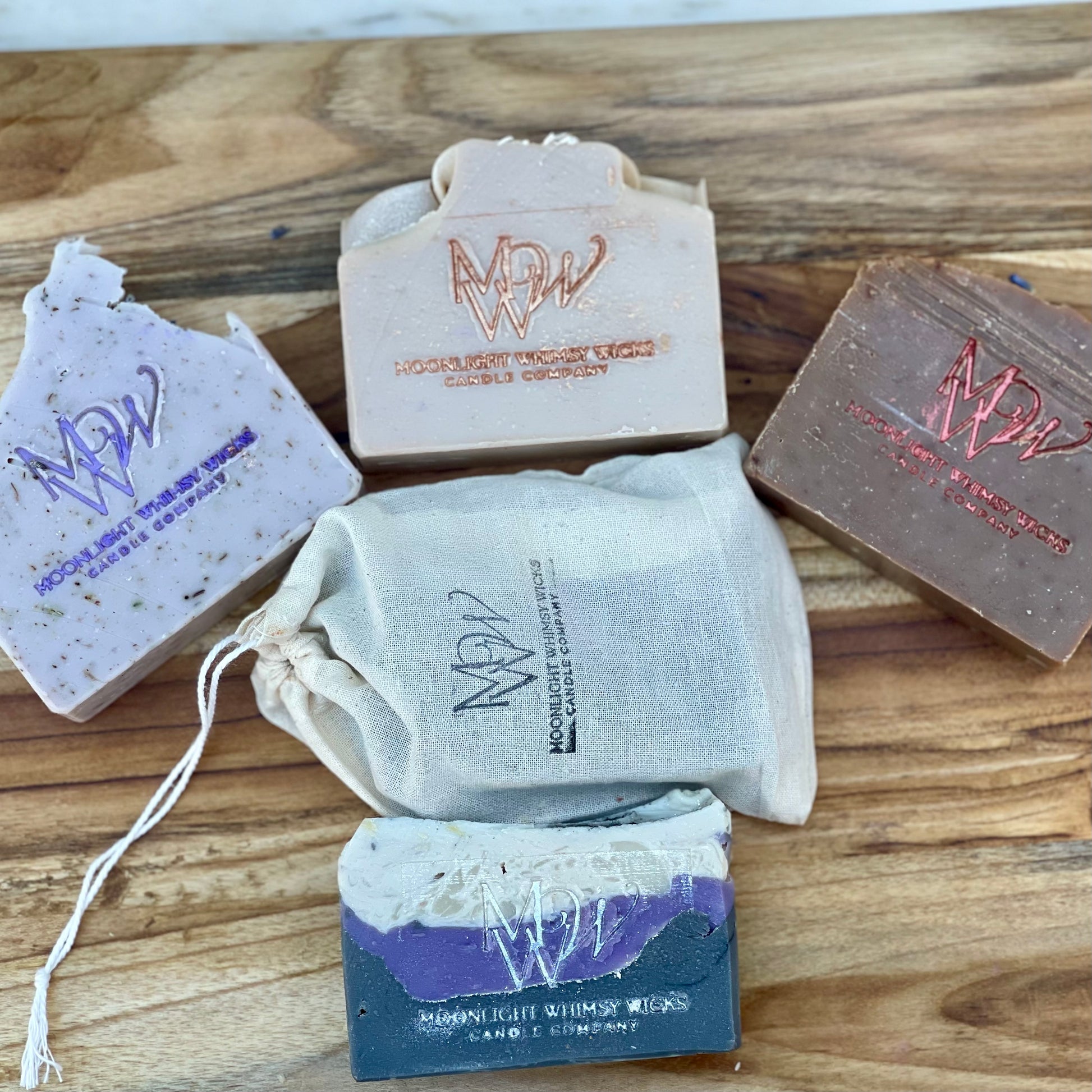 Artisan handmade soap bars from Moonlight Whimsy Wicks displayed on a wooden board, featuring cold processed soap, and a muslin gift bag. Small batch, eco-friendly bar soaps for sensitive skin and luxury skincare routines.