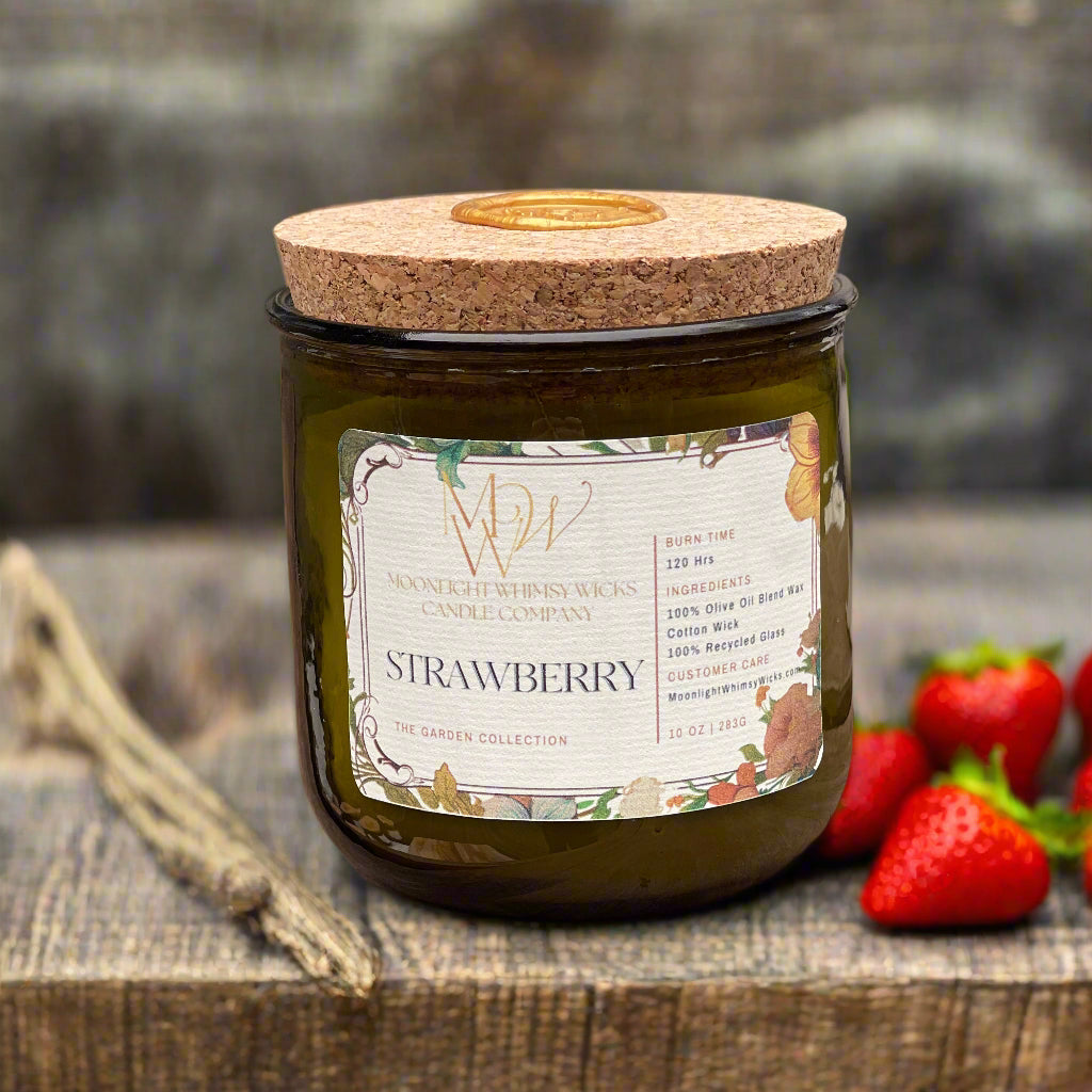 Strawberry Candle from Moonlight Whimsy Wicks’ Garden Collection, styled in a green recycled glass jar with a cork lid and floral label on a rustic surface with strawberries
