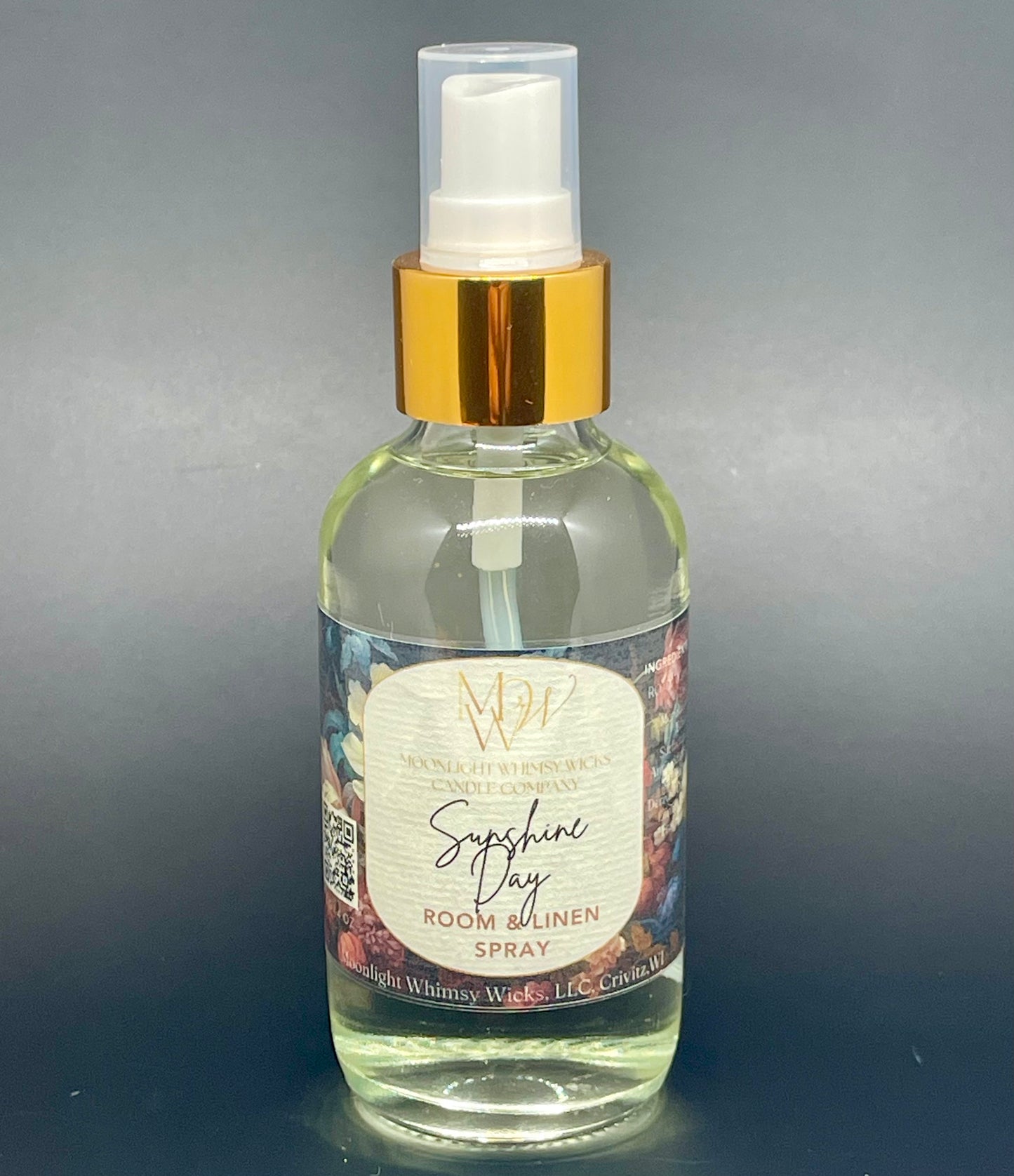 Clear spray bottle with gold cap labeled 'Sunshine Day Room & Linen Spray' on a gray background