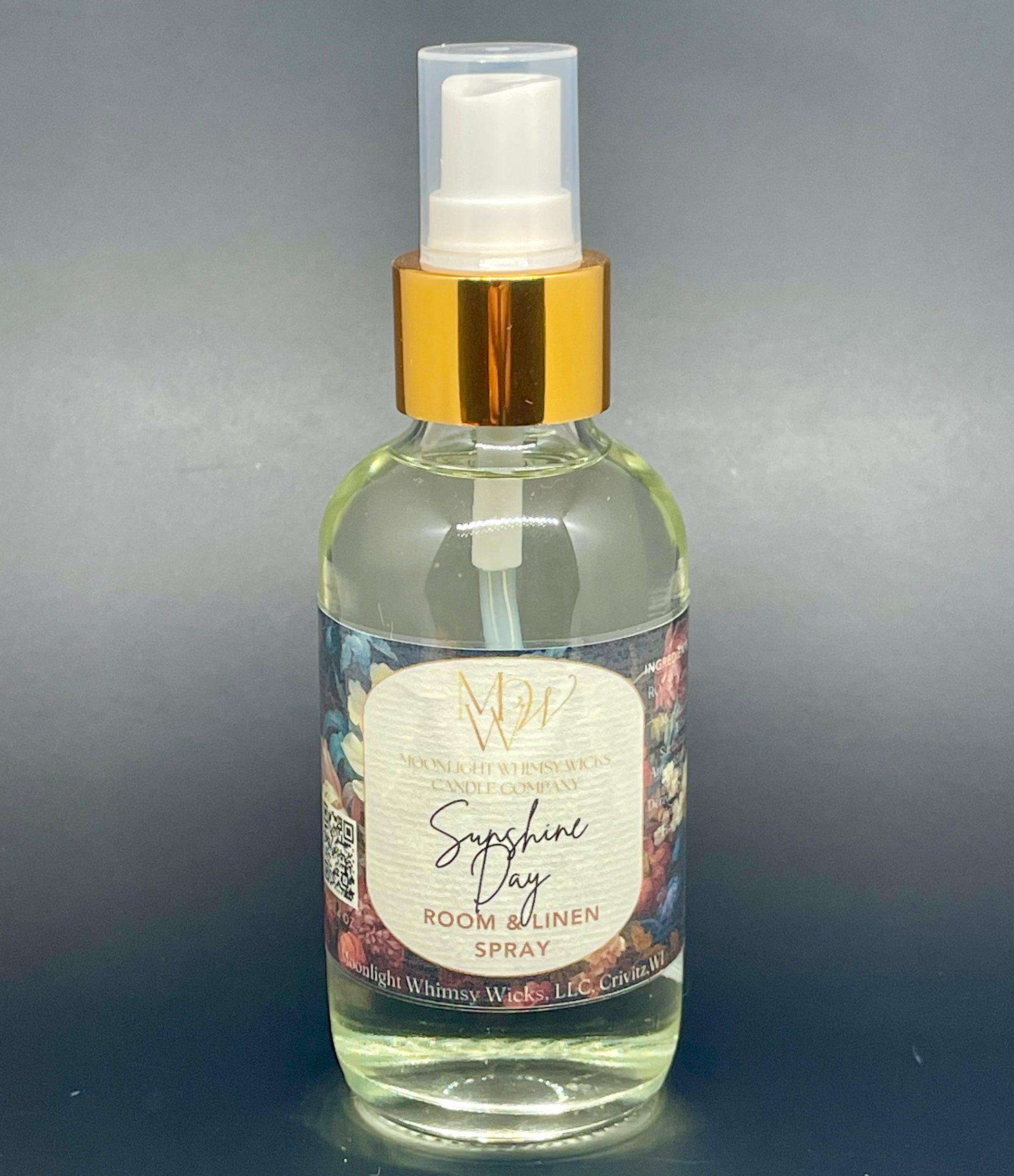 Clear spray bottle with gold cap labeled 'Sunshine Day Room & Linen Spray' on a gray background