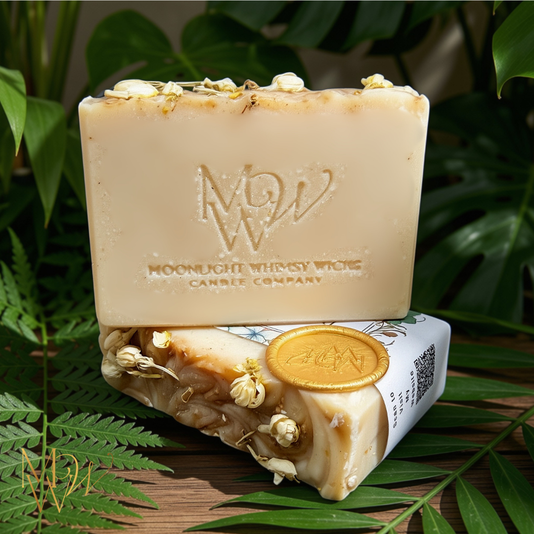 A creamy white bar of soap with white jasmine buds on top and a Moonlight Whimsy Wicks stamp surrounded by green palm leaves.