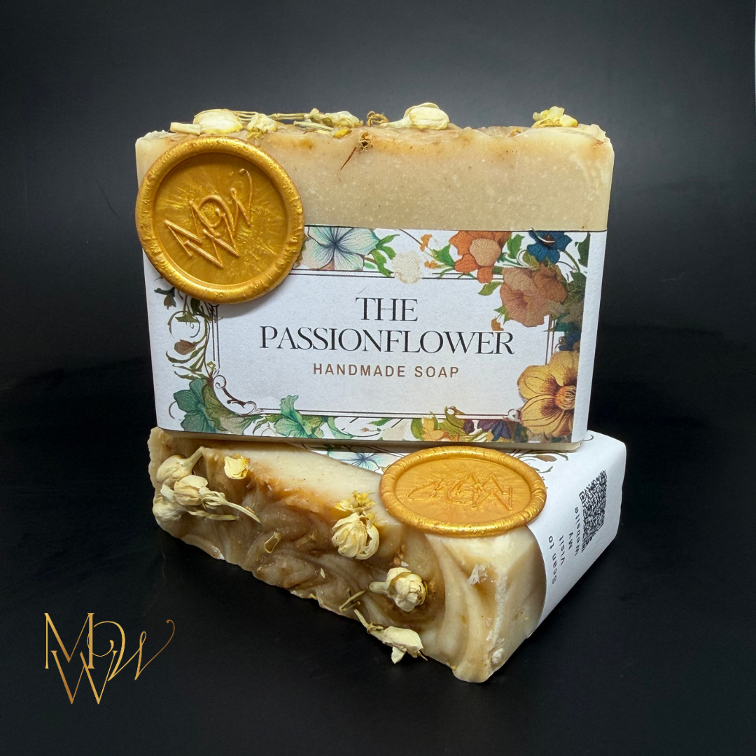 A creamy white bar of soap on a black background.  A floral band labeled The Passionflower with a gold wax seal by Moonlight Whimsy Wicks.