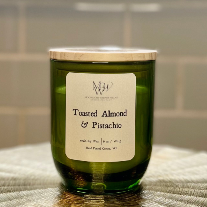 Green candle labeled 'Toasted Almond & Pistachio' on a textured surface with a tiled wall background.