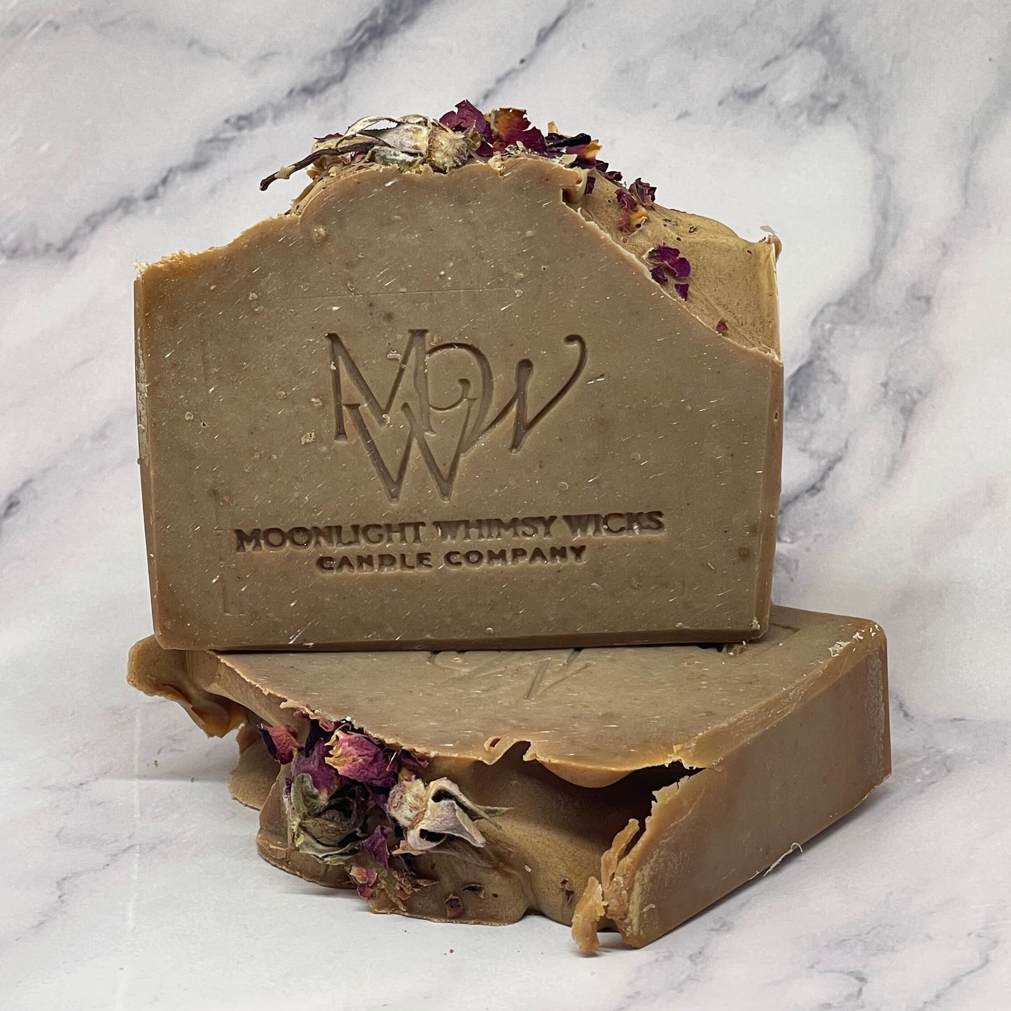Two brown soap bars with floral elements on a marble surface, featuring the Moonlight Pottery Works logo.