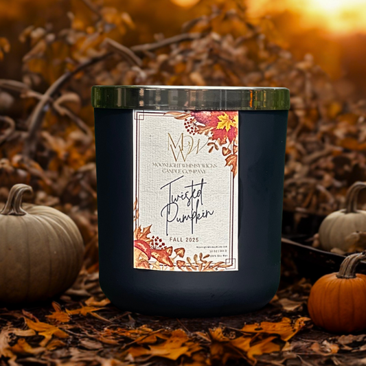 Twisted Pumpkin candle by Moonlight Whimsy Wicks, shown in a matte black jar with botanical label, nestled among fallen autumn leaves and pale pumpkins at golden hour.
