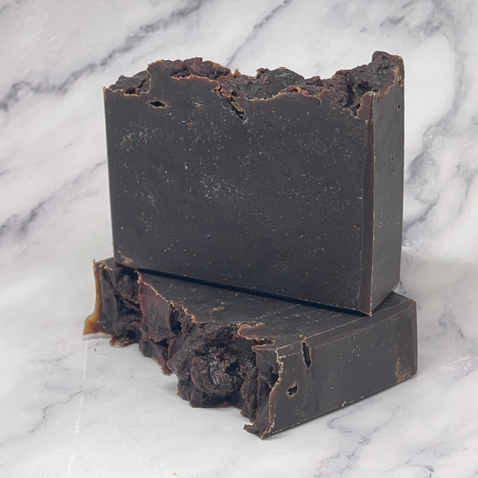 Two bars of dark brown soap on a marble surface