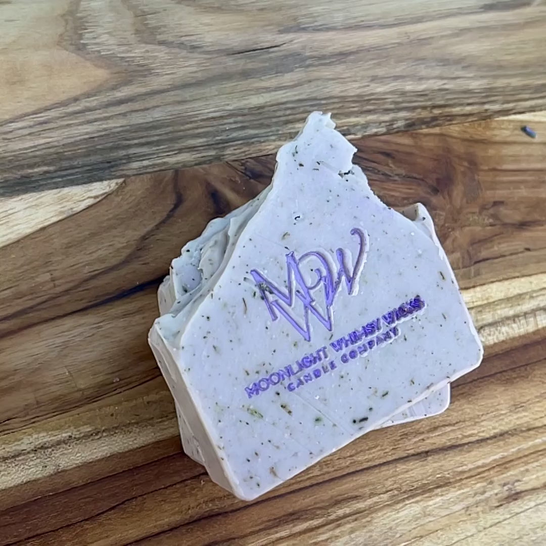 Close-up video of Moonlight Whimsy Wicks handmade lavender soap bar with purple logo, cold processed and infused with natural botanicals and exfoliating herbs. Artisan soap for sensitive skin, crafted in small batches for natural skincare routines