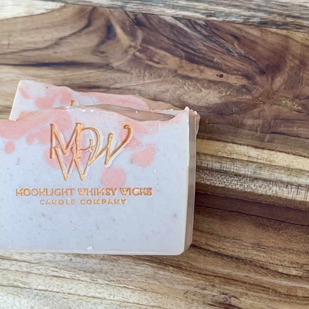 Short, Close up video of Moonlight Whimsy Wicks handmade artisan soap bar with warm orange swirls and gold foil logo, crafted using the cold process method. Small batch natural soap with a soft citrus scent and gentle exfoliating texture, ideal for daily skincare.  Inspired by Bitter Peach.