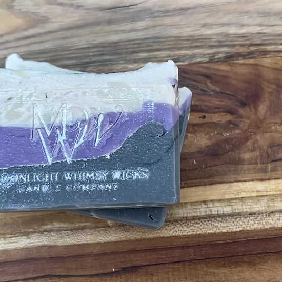 Close up video of Moonlight Whimsy Wicks artisan soap bar with dramatic layers of charcoal black, lavender purple, and creamy white. Handmade cold processed soap.