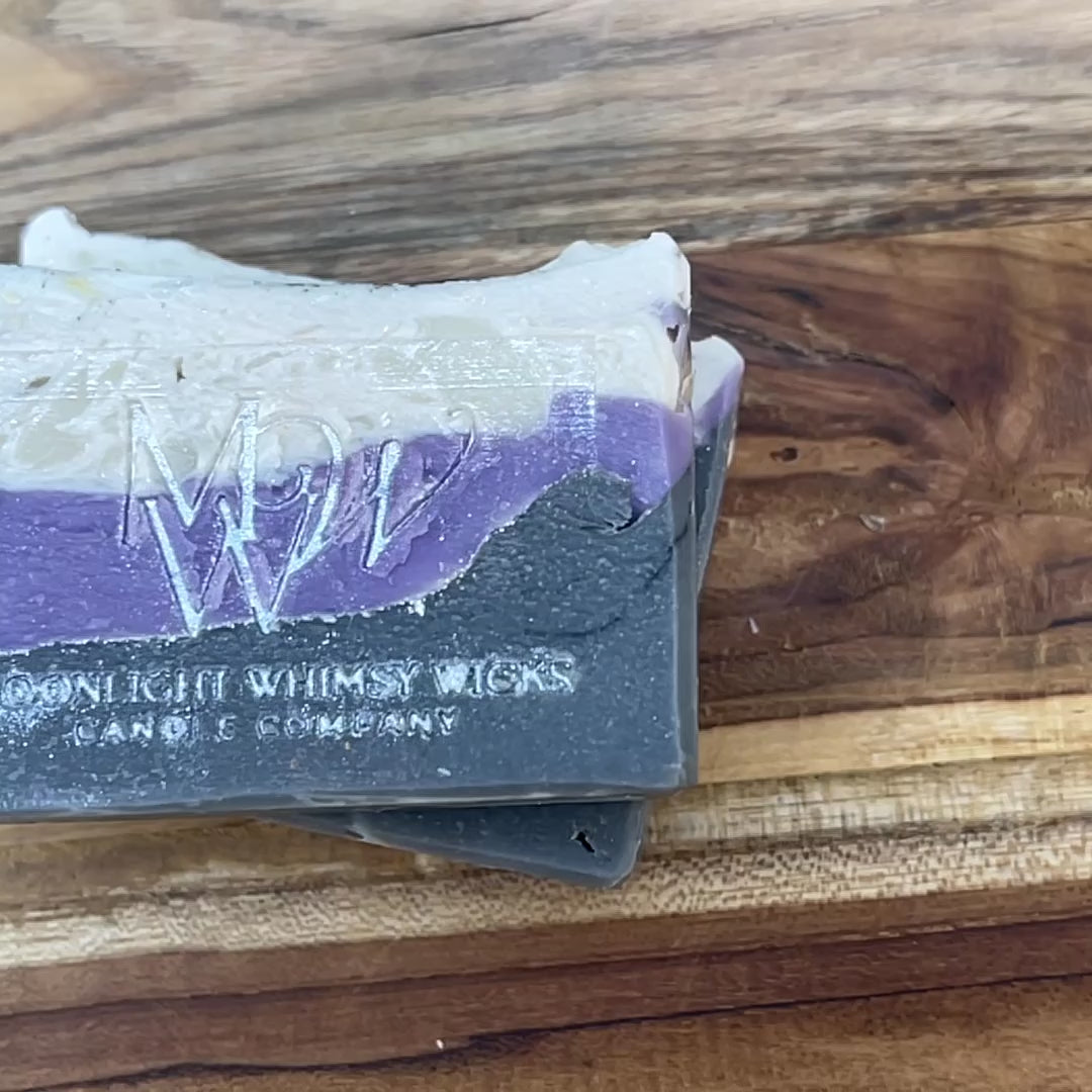 Close up video of Moonlight Whimsy Wicks artisan soap bar with dramatic layers of charcoal black, lavender purple, and creamy white. Handmade cold processed soap.